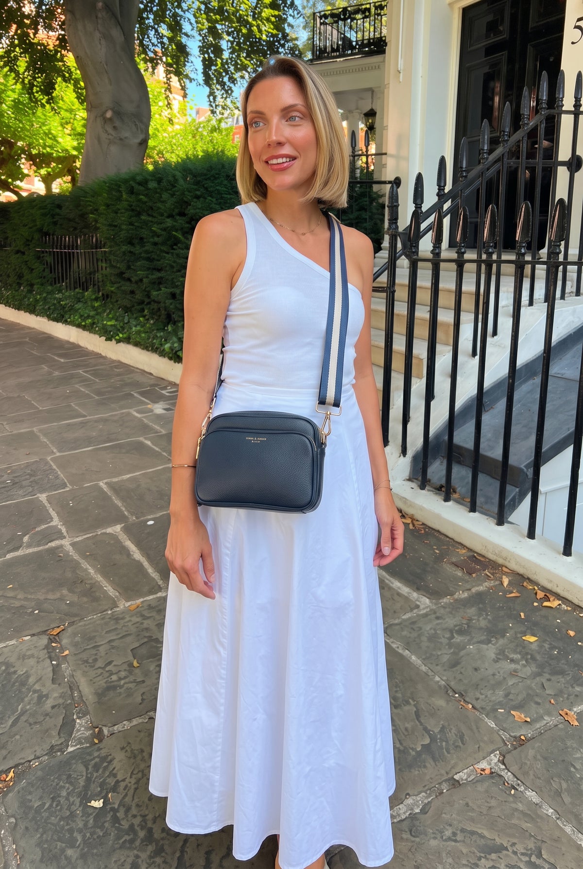 Woman in a white dress wearing a navy Sofia and Spritz crossbody bag on a London street